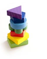 Stack of colorful wooden toy blocks in an assortment of different basic shapes for teaching children over a white background with copy space