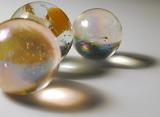 Trio of toy glass marbles casting artistic ring form shadows over a grey background with copy space