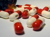 Red and White Medication Capsules Spilled from Fallen Open Prescription Pill Bottle on White Background