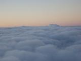 Flying above the clouds with a colourful sunset or sunrise visible over a dense blanket of white clouds