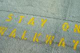 Stay on Walkway street sign stencilled on a road surface in yellow paint as a warning to pedestrians