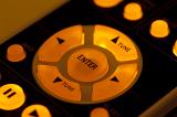 Yellow glowing backlit buttons of remote control, close-up cropped image of arrows and Enter button