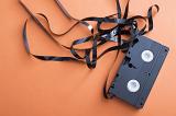 Damaged video cassette with uncoiled tape in a tangled mess over an orange background with copy space in a communications and entertainment concept