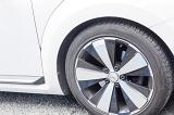 Modern low profile car tyre with alloy rim with white spokes on a white vehicle parked on tarmac, close up view