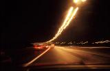 Traffic blur on a highway at night with a curving row of illuminated street lamps disappearing into the distance with motor vehicles in motion