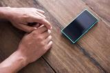 A man rests his hands on a timber bench top as he waits for a text message to appear on a blank smart phone.